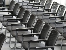 Row of empty black chairs with armrests in a waiting area.
