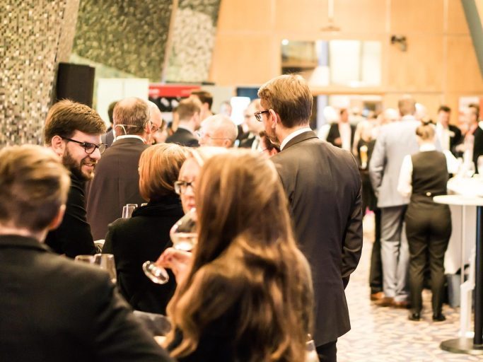 A group of people in formal attire socialising at an indoor event.