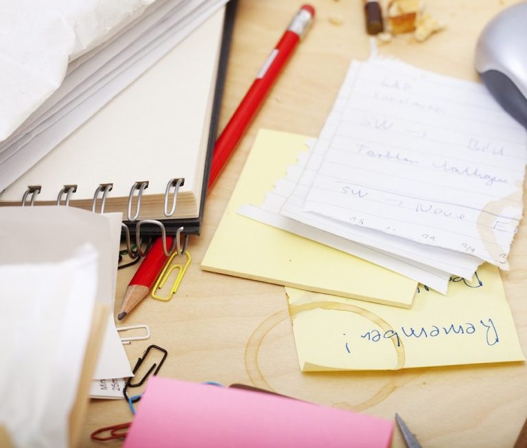 Scattered papers, sticky notes, a notebook, and a pen on a wooden desk.